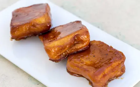 Tres torrijas de miel, doradas y brillantes, reposan en un plato blanco.