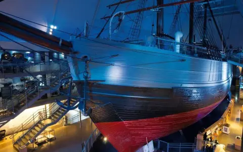 Ein historisches **fram schiff** mit Anker, umgeben von Treppen und Ausstellungsbereichen, in blauem Licht.