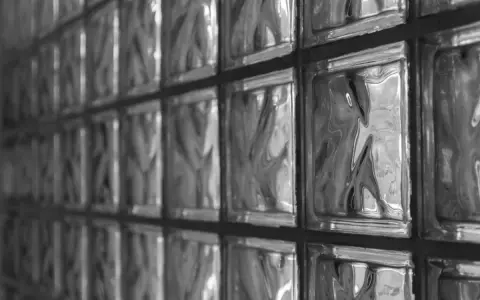 Muro con vetrocemento, una texture di blocchi di vetro che riflettono la luce creando un gioco di ombre e riflessi.