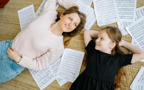 Mutter und Tochter liegen auf Notenblättern und lächeln sich an. Ein friedlicher Moment, der zeigt, wie Musik im Alltag verbindet.