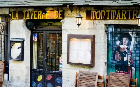 La taverne de Montmartre, une définition de l'ambiance parisienne. Façade de pierre, enseigne jaune, menu affiché, et une peinture murale d'un mousquetaire.