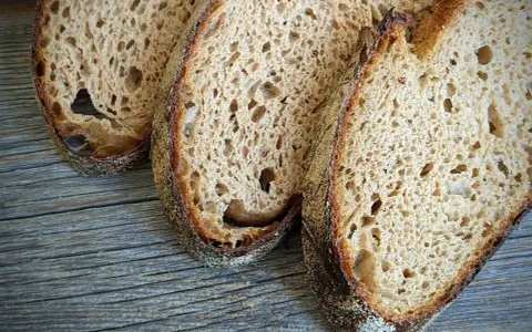 Drei Scheiben rustikales Sauerteigbrot liegen auf Holz. Der Sauerteig ist zu sauer, aber die Kruste ist perfekt gebräunt.