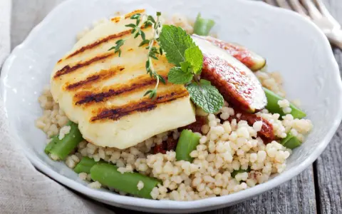 Kuskus z grillowanym serem halloumi, fasolką szparagową i figami, ozdobiony miętą.