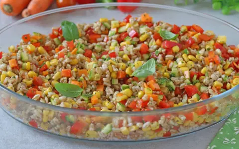 Insalata di farro colorata con mais, peperoni, zucchine e carote, guarnita con foglie di basilico fresco. Un piatto estivo e salutare.