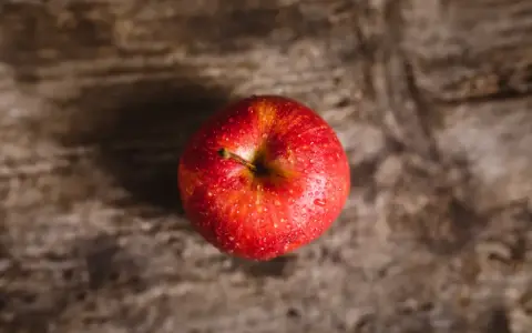 Czerwone jabłko z kroplami wody na drewnianym tle.