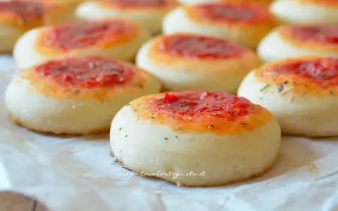 Pizzette fatte in casa, piccole e invitanti, con un soffice impasto e un tocco di pomodoro e erbe aromatiche.