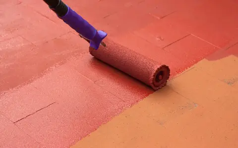 Rodillo pintando suelo de patio exterior con pintura roja, renovando el espacio.