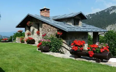 Charmante maison en pierre avec cheminée, entourée de fleurs rouges. Idéale pour ma prime rénov résidence secondaire.