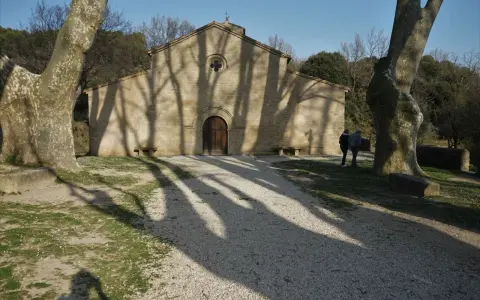 L'église de Vaugines, baignée de soleil, accueille deux visiteurs. Les ombres des arbres dansent sur sa façade de pierre.