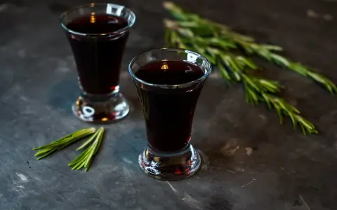 Dwa kieliszki ciemnego, aromatycznego nalewki z czernic, ozdobione gałązkami rozmarynu.