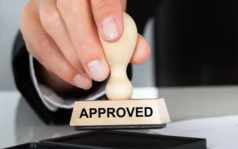 Dłoń z pieczątką "APPROVED" nad poduszką z tuszem. To symbol zatwierdzenia, jak certyfikat AEO.