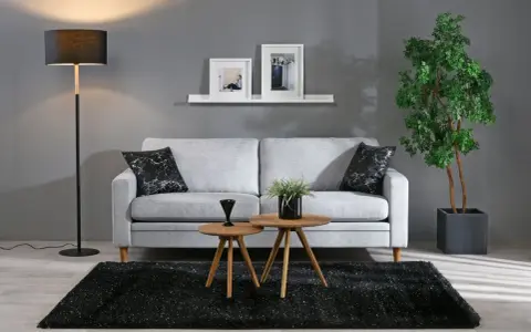 En stilren inredning grått med en ljusgrå soffa, svart matta och en golvlampa. Två runda bord framför soffan.