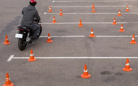 Motocyklista w kasku pokonuje tor przeszkód z pachołków, ćwicząc jazdę na prawo jazdy **kategoria a2**.
