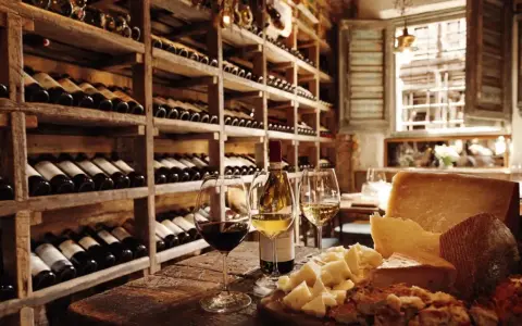 Regal gefüllt mit italienischem Wein, daneben Gläser mit Rot- und Weißwein, Käse und Brot auf einem Holztisch.