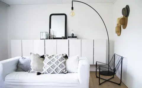 En stilren och modern manlig inredning med vit soffa, svarta detaljer och en golvlampa.