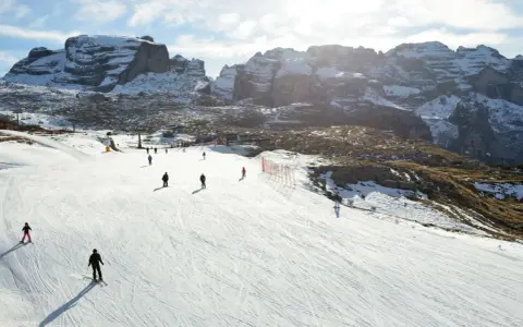 Narciarze szusują po ośnieżonym stoku w Dolomitach. Idealne miejsce, gdzie na narty we Włoszech, z majestatycznymi górami w tle.