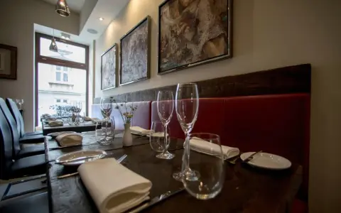 Elegancko nakryte stoły w restauracji z gwiazdką Michelin w Polsce. Czerwone obicia, obrazy na ścianach i kieliszki zapraszają na wyjątkowe doznania kulinarne.