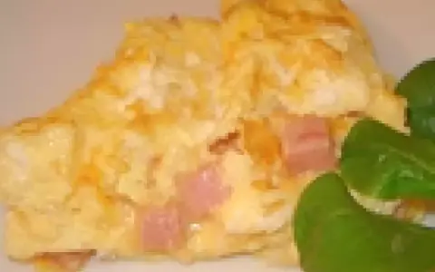 Une omelette jambon fromage dorée, garnie de dés de jambon rose et de fromage fondant, accompagnée de quelques feuilles vertes.
