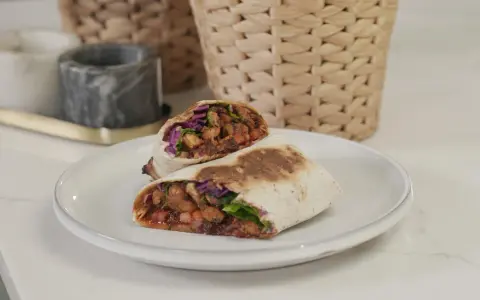 Kebab zawinięty w tortillę, przekrojony na pół, z widocznym nadzieniem z mięsa, warzyw i sosu.