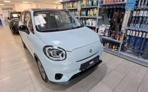 Jasnoniebieski Leapmotor T03 stoi w salonie samochodowym obok półek z akcesoriami.