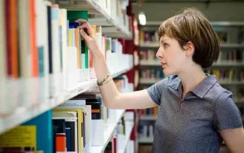 Kobieta, która wygląda jak bibliotekarz, wybiera książkę z półki w bibliotece.