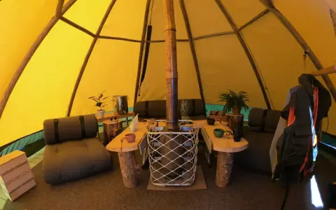 Mysig interiör i ett tipi-tält på Sorsele camping. Här finns sittplatser, ett bord och en kamin för värme.