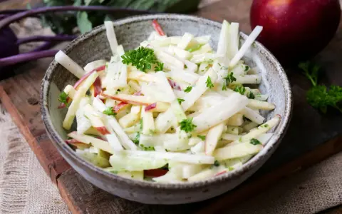 Kohlrabi Salat mit Apfelstücken und frischer Petersilie, garniert mit einem roten Apfel im Hintergrund.