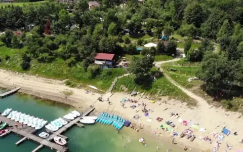 Polańczyk plaża tętni życiem. Ludzie odpoczywają na piasku, a na wodzie czekają rowery wodne i kajaki.