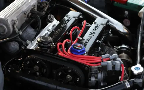 Motor de coche con tapa de válvulas "16 VALVE", cables rojos y correa de distribución.