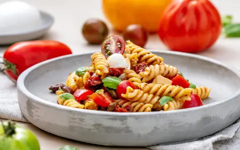 Ein köstlicher italienischer Nudelsalat mit Fusilli, Tomaten, Mozzarella und Basilikum auf einem grauen Teller.