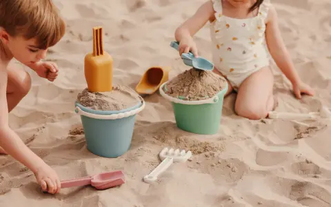 Niños disfrutando de juegos en la playa con cubos y palas de arena.