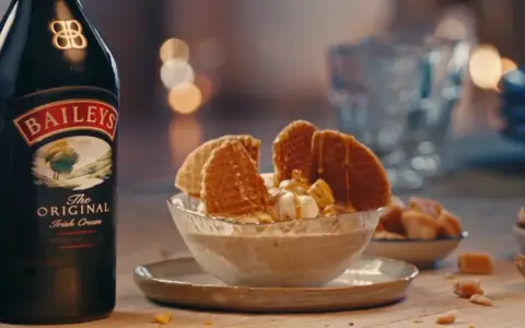Baileys Eis Rezept: Cremiges Eis mit Karamell und Waffeln, daneben eine Flasche Baileys.