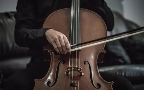 Eine Hand hält den Bogen über dem Violoncello-Instrument, bereit, die Saiten zum Klingen zu bringen.