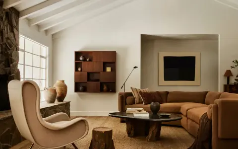 Un acogedor salón con chimenea de piedra, sillón de tela, sofá marrón y mesa de centro de madera. El arte de pared y las cerámicas añaden un toque de estilo chino hogar.