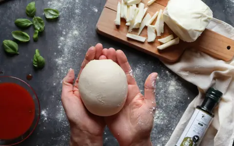 Hände formen Teig für ein Caputo Nuvola Rezept. Mozzarella, Basilikum und Tomatensauce liegen bereit.