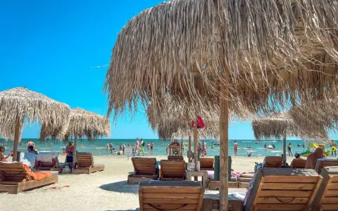 Słoneczny dzień na plaży w Rumunii nad Morzem Czarnym. Leżaki i parasole z trawy zapraszają do odpoczynku.