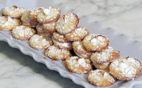 En hög med spröda småkakor, pudrade med florsocker, som doftar härligt av amaretto smak.