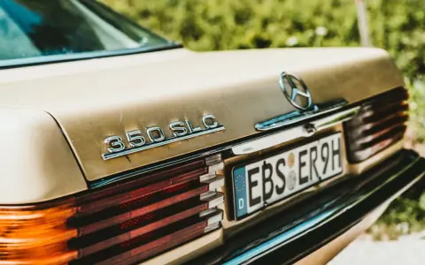 Detalle de un Mercedes 350 SLC dorado, con la luz de matrícula visible, listo para pasar la ITV.