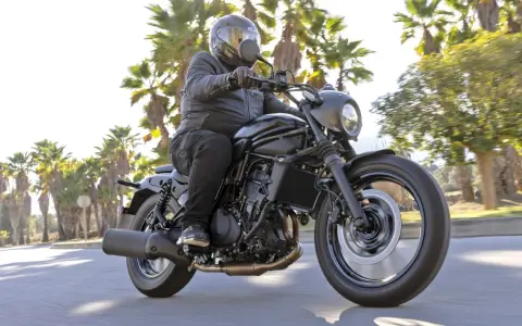 Mężczyzna w kasku jedzie czarnym motocyklem Kawasaki EN 500. Wady i zalety tego modelu są dyskutowane podczas jazdy wśród palm.