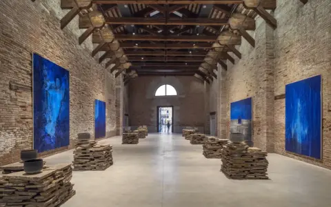 Vaste salle d'exposition à Venise, avec des œuvres d'art bleues et des sculptures en pierre. L'architecture industrielle de Pinault Venise est mise en valeur.