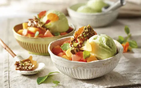 Deliciosos postres saludables: helado verde cremoso con trozos de melón, papaya y un toque crujiente de pistachos.