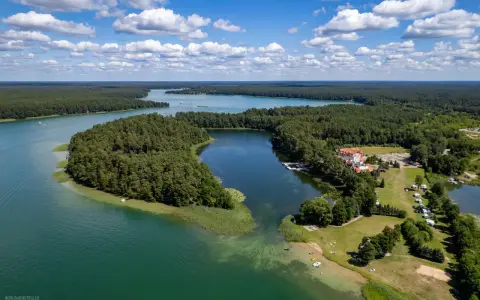 Malownicze jezioro Urszulewskie otoczone lasem, z hotelem i polem namiotowym na brzegu.