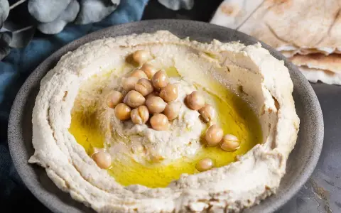 Krämig hummus med kikärtor och olivolja, perfekt för ett enkelt hummus recept. Serveras med pitabröd.