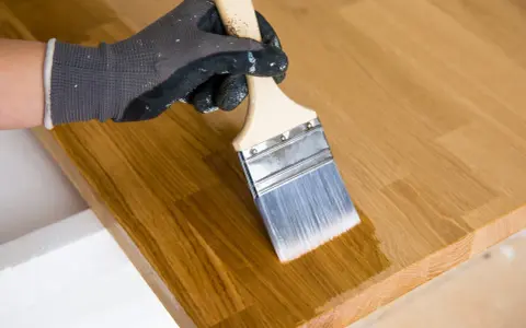 Main tenant enlever huile de lin sur bois avec un pinceau. Le bois est clair et le pinceau applique une couche protectrice.