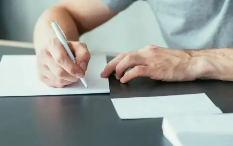 Mężczyzna pisze ręcznie list motywacyjny, przygotowując się do ważnego spotkania.