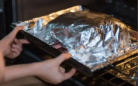 Mains dans un plat recouvert d'aluminium au four, prêt à cuire.