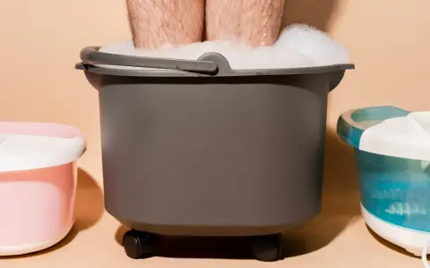 A person's legs are submerged in a foamy foot bath, part of a home foot detox setup with other foot spa machines.