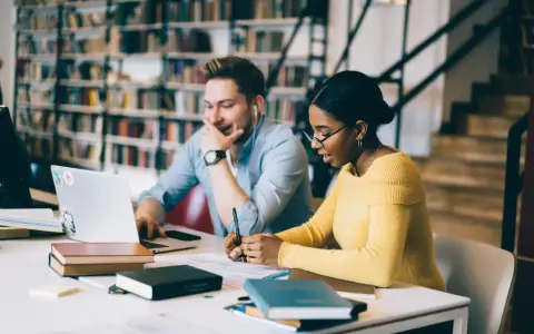 Studenti universitari collaborano a un progetto, immersi in libri e tecnologia.