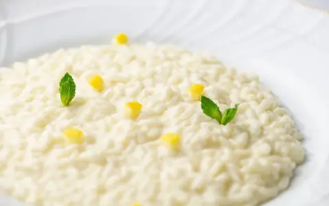 Un cremoso risotto al limone, guarnito con cubetti di limone e foglie di menta fresca, pronto per essere gustato.