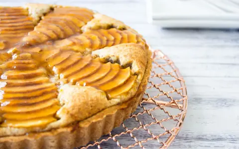 Deliciosa tarta de pera francesa, con peras laminadas y glaseado dorado, enfriándose sobre una rejilla de cobre.